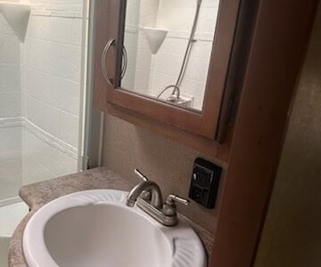Bathroom sink with faucet and mirror above, shower with glass door in background.