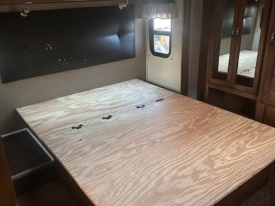 RV bedroom with unfinished wooden bed frame, window, and wardrobe.