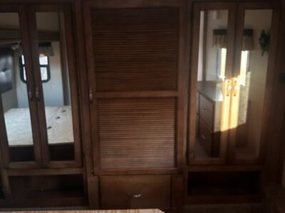 Wooden closet with mirrored sliding doors and louvered panel in a bedroom.