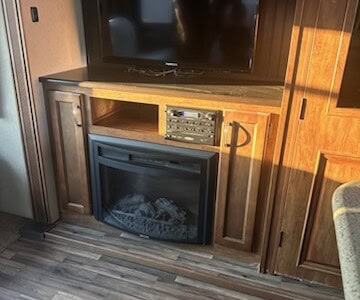 Large flat-screen TV above electric fireplace in wooden entertainment unit.