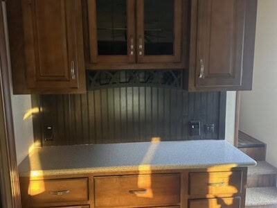 Wooden kitchen cabinets with glass doors and drawers, dark wood finish, in a modern kitchen setting.