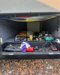 Open utility truck storage box with tools, cables, and equipment inside.