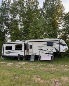 2021 Chamberlain fifth wheel RV with slide-outs and modern exterior design, parked on grassy area with trees in background.