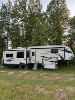 2021 Chamberlain fifth wheel RV with slide-outs and modern exterior design, parked on grassy area with trees in background.