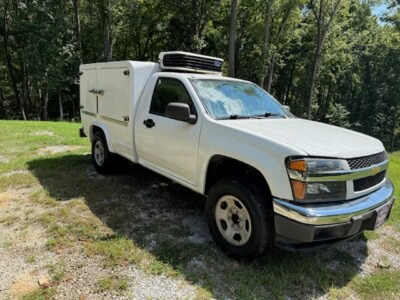 2012 Chevrolet Colorado utility vehicle with refrigeration unit in a wooded area.