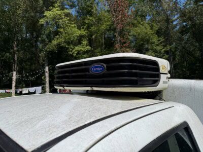Carrier rooftop air conditioning unit mounted on vehicle roof with trees in background.