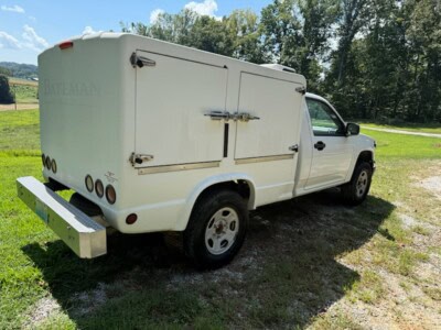 2000 Bateman utility truck with enclosed cargo area and rear bumper, parked on grassy field.