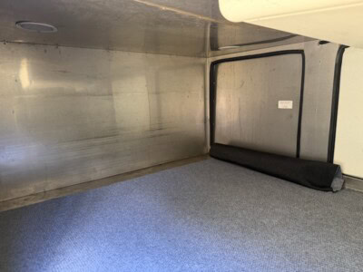 Interior of aluminum cargo trailer with gray carpeted floor and black rolled-up mat.