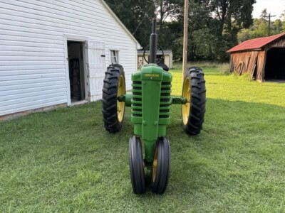Green John Deere Model B tractor with large rear tires and smaller front tires on a grassy field.