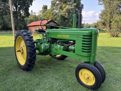 Green 1947 John Deere B tractor with yellow wheels on grassy field.