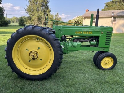 Vintage 1947 John Deere B tractor with green body and yellow wheels on grassy field.