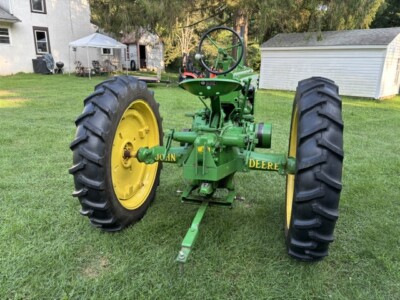 Vintage 1947 John Deere B tractor with large rear tires and green body in a backyard setting.