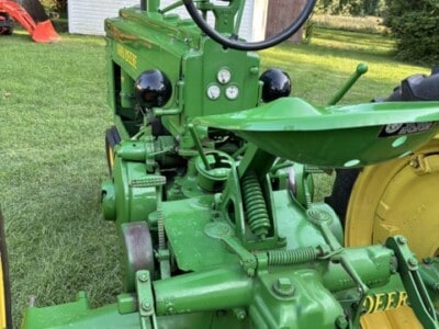 Green John Deere tractor with steering wheel, controls, and yellow wheel in a grassy yard.