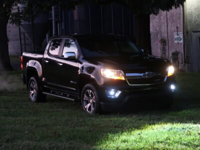 2018 Chevrolet Colorado Z71 black pickup truck with headlights on on grassy area at night.