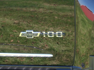 Chevrolet 50th anniversary emblem on vehicle with green grass reflection.