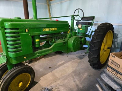 1948 John Deere B tractor with green body and yellow wheels, front grille, and seat in a storage area.