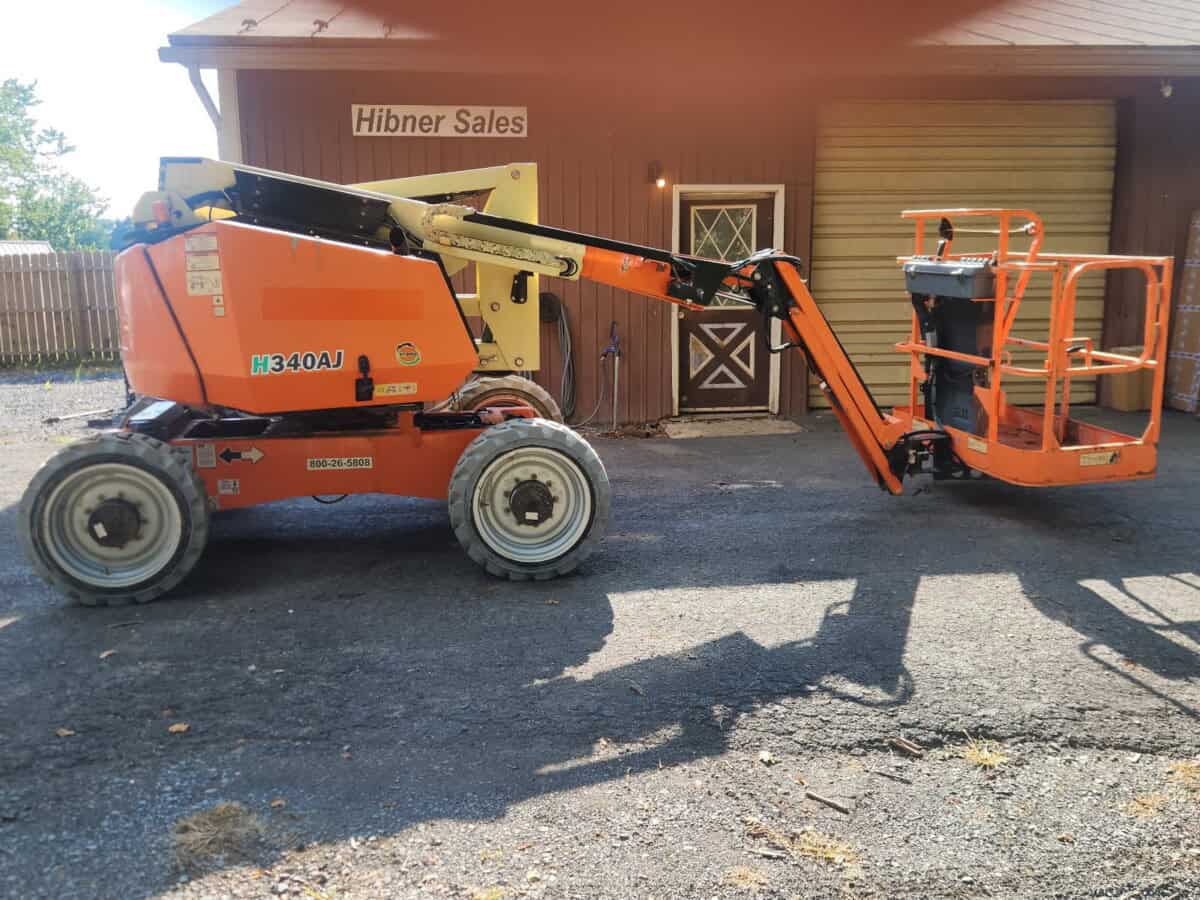 2019 JLG 340AJ boom lift with orange platform and black arm, parked outside a building with Hibner Sales sign.