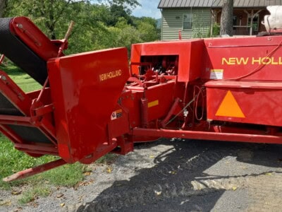 New Holland 565 forage harvester with red body and large wheels on grassy field.