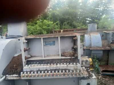 Heavy industrial machinery with rust and dirt, outdoor setting with trees in background.