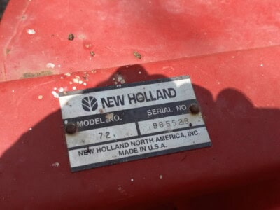 New Holland 565 model serial plate on red equipment with grass background.