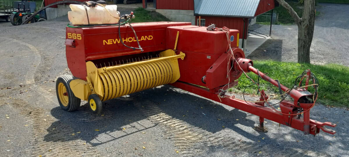 Red New Holland 565 hay conditioner with yellow rollers and hitch for tractor attachment.