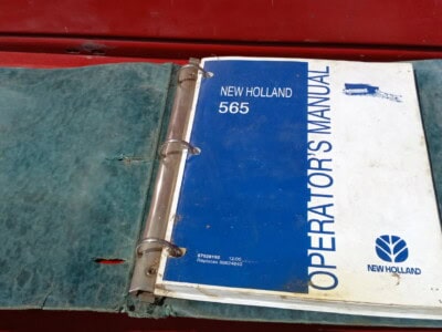 Open New Holland 565 operator's manual on red surface.
