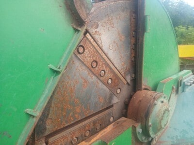 Rusty metal machinery part with green and blue paint, visible bolts and rusted surface.