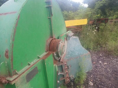 Green agricultural equipment with rusted parts and overgrown vegetation.