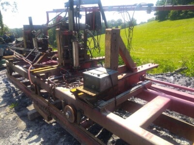 Red circular sawmill with hydraulic components and metal frame on a grassy field.