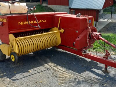 Red New Holland 565 hay conditioner with yellow rollers and hitch for tractor attachment.