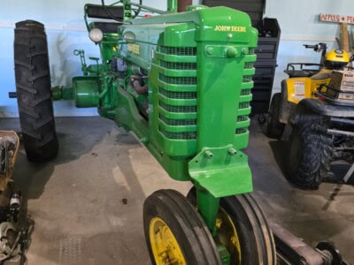 1948 John Deere B tractor with green body and yellow wheels, vintage farm equipment, in indoor storage.