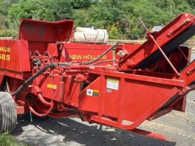 New Holland 565 forage harvester with conveyor and large tires on gravel surface.