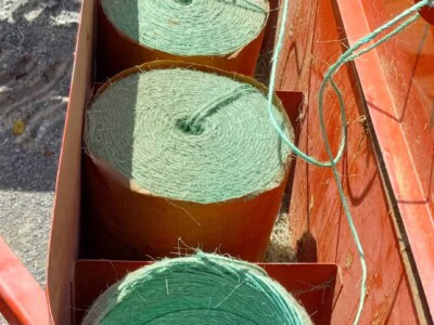 Four green cylindrical bales of hay in a red hay baler machine.