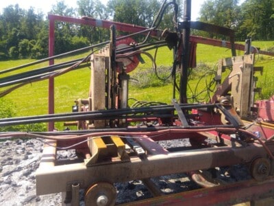 Heavy-duty industrial sawmill equipment with hydraulic components and metal frame on a grassy field.