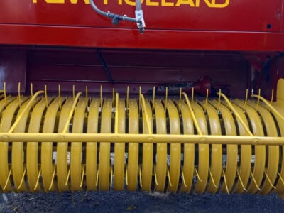 New Holland 565 hay rake with yellow tines and red frame for farm hay collection.