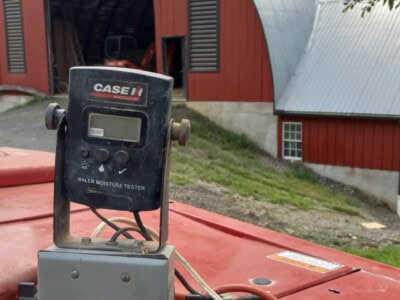 Case IH Bale Moisture Tester device on agricultural equipment with red barn in background.
