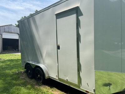 Green enclosed aluminum concession trailer with side door and dual axles on grassy area.