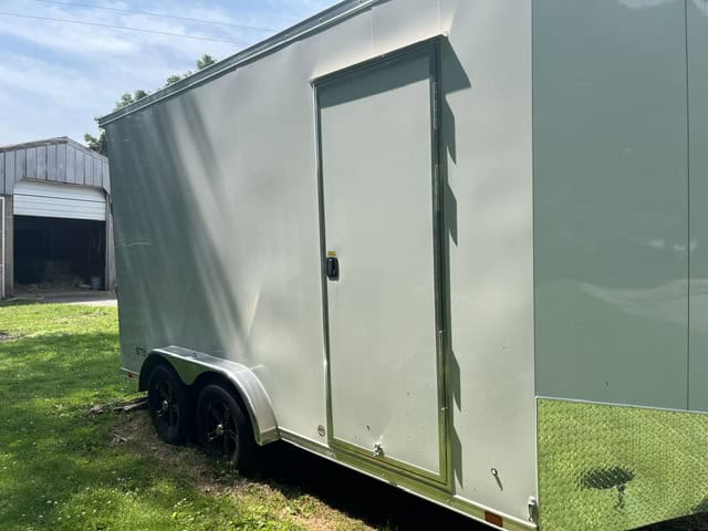 Green enclosed aluminum concession trailer with side door and dual axles on grassy area.