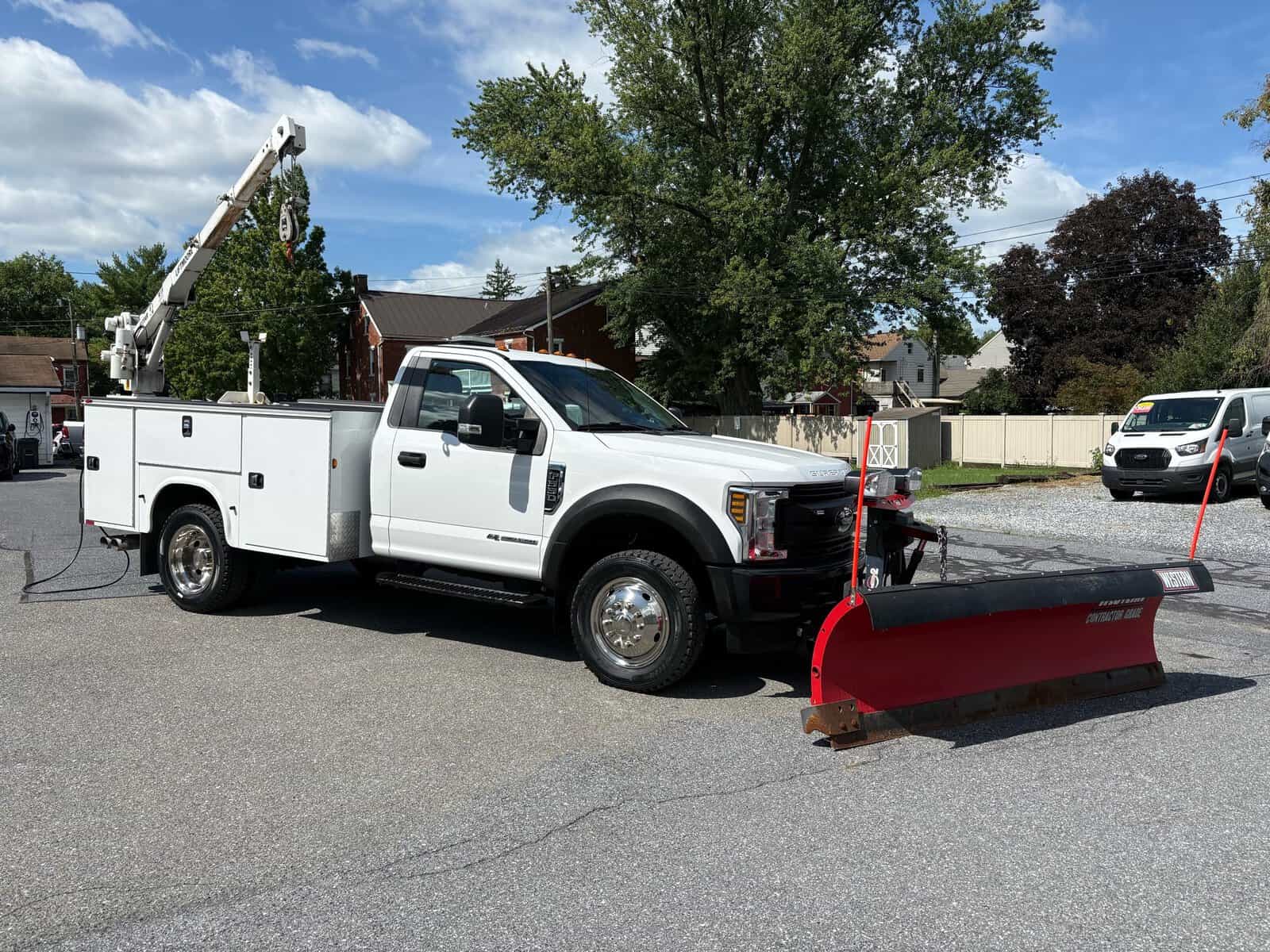 10946 - 2018 Ford F-550 Chassis - 012 White utility truck with snow plow attachment and bucket lift on a residential street.