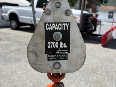 Lifting block with 2700 lbs capacity and 15 lbs hook weight, outdoors with vehicles and trees in background.