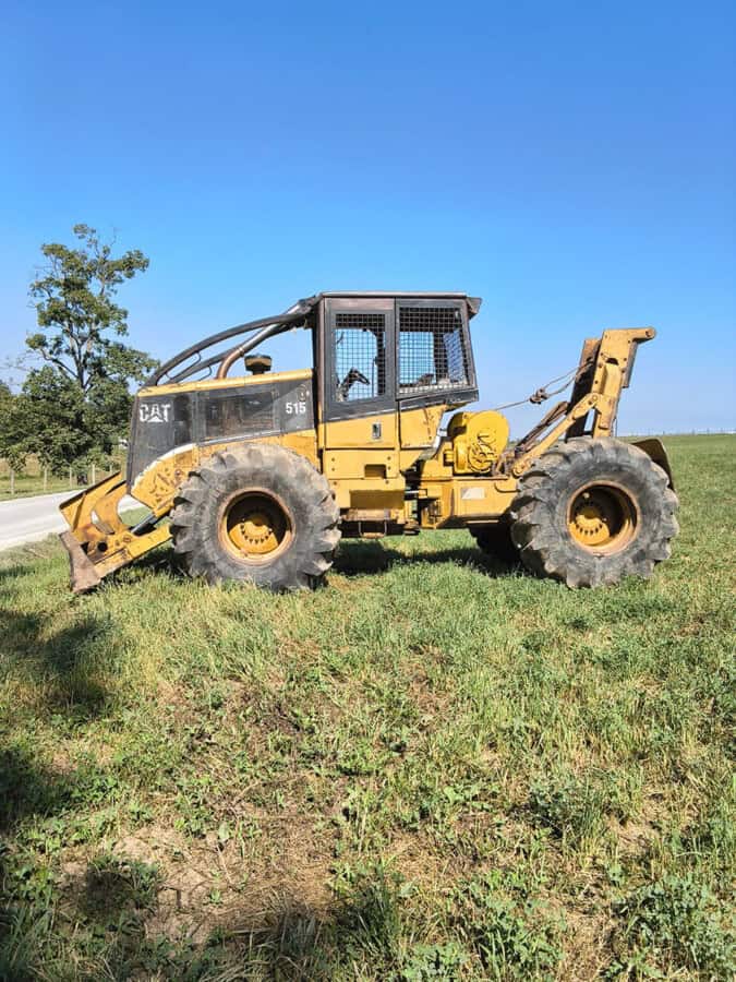 Caterpillar 515 skid steer loader with yellow body and black cab on grassy field under blue sky.