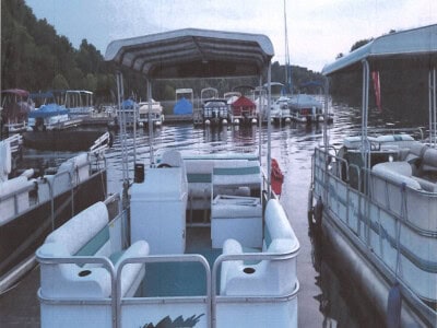 Pontoon boat with canopy on lake, surrounded by other boats and watercraft, calm water, trees in background.
