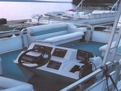 Pontoon boat with seating, steering console, and canopy on calm water.