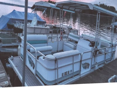 Suncruiser pontoon boat with canopy, seating, and safety rails on dock at sunset.