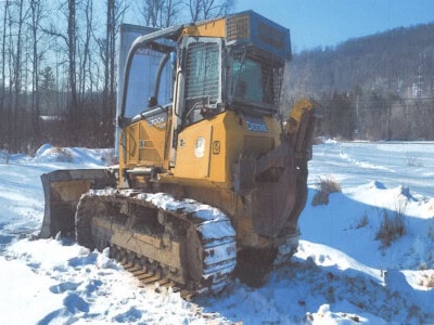 Caterpillar D5K2 LGP tracked loader with cab in snowy landscape, winter condition, visible tracks and blade attachment.