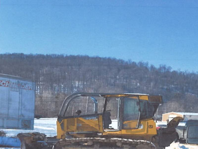 Yellow Caterpillar 700K track loader with enclosed cab on snowy ground under clear blue sky.