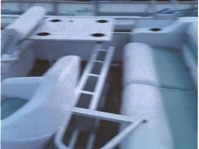 Pontoon boat interior with seating, ladder, and deck features in a marina setting.
