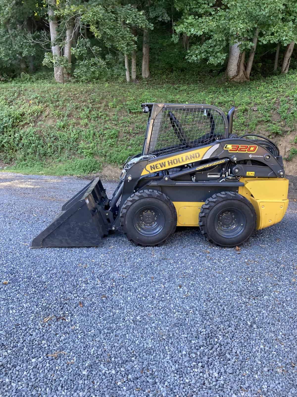 IMG_0009 (1) New Holland L320 skid steer loader with black and yellow body and bucket attachment on gravel surface.