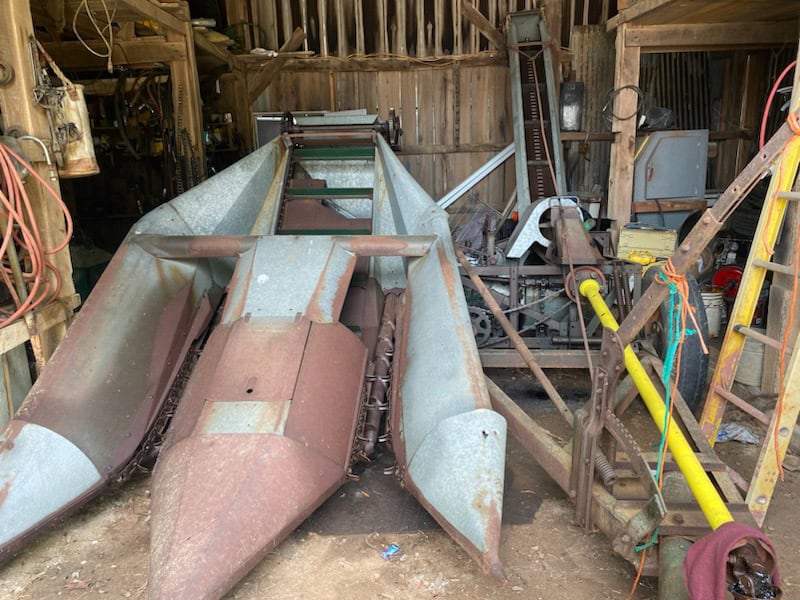 Rusty vintage farm equipment with metal frame and blades in barn setting.