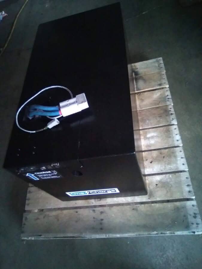 Large black industrial battery pack with wiring on wooden pallet in warehouse.